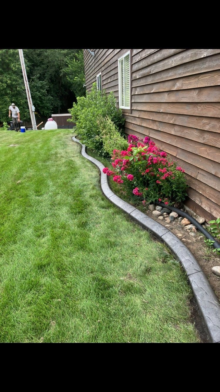 Installer laying concrete curbing along a foundation bed